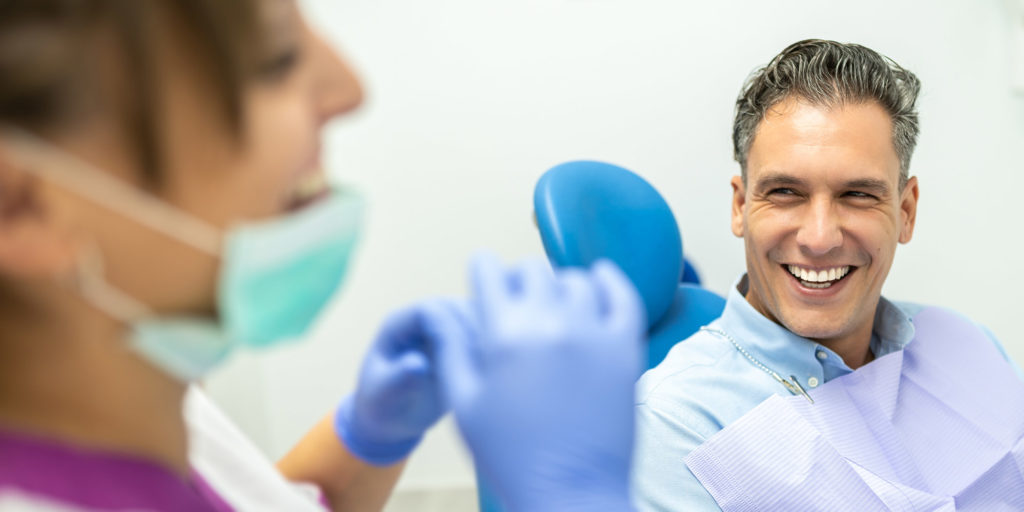 Nice guy smiling in dental chair looking at dental assistant