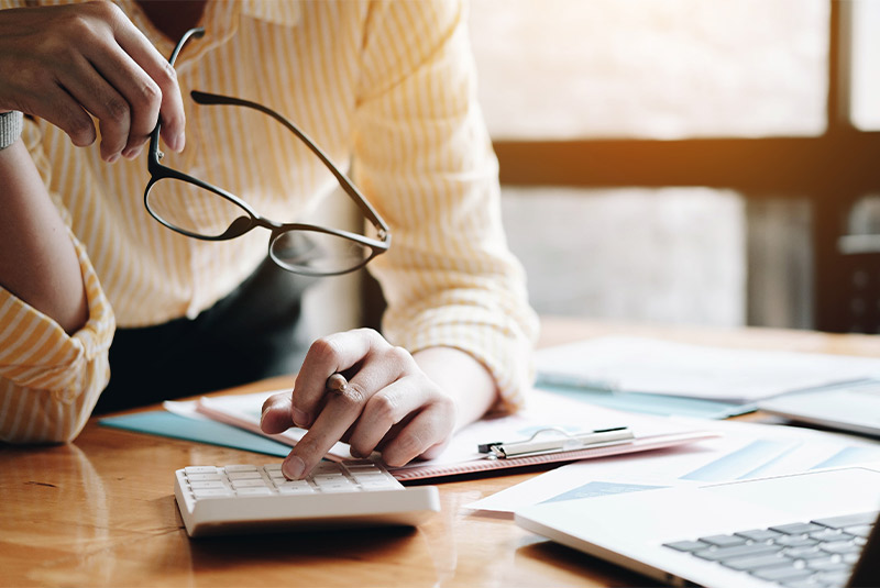 N ice lady wearing yellow and white striped shirt holding glasses typing into calculator
