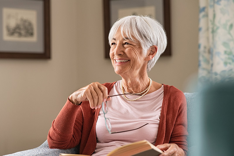 Very nice lady with white hair smiling looking to the side holding a book in one hand and her glasses in the other hand